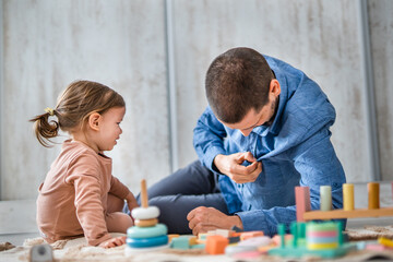 Naklejka premium One man caucasian playing at home with his daughter toddler on the floor with wooden toys, modern parenthood lifestyle single parent concept 
