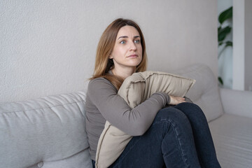 Depressed single young woman holding pillow going through emotional crisis after abuse abortion sitting on couch at alone home. depression concept.