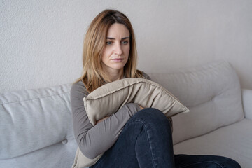 Depressed single young woman holding pillow going through emotional crisis after abuse abortion sitting on couch at alone home. depression concept.