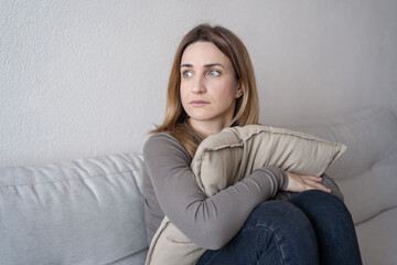 Obraz premium Portrait of lonely sad сaucasian young woman sitting on couch and hugs pillow.