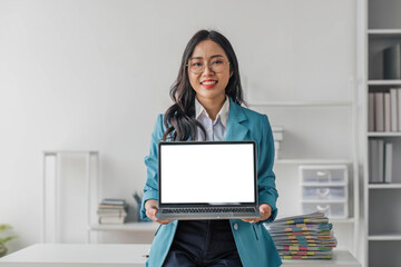 Happy asian business woman holding laptop with blank screen stands in a modern office looking at...