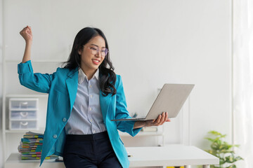 Beautiful Asian girl celebrate with laptop, success happy pose. E-commerce, university education, internet technology, or startup small business concept. Modern office or living room with copy space