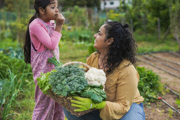 Happy indian mother having fun gardening with little daughter - Harvest and organic food concept