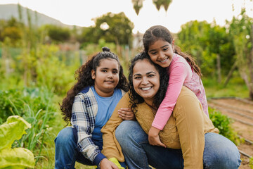Fototapeta premium Happy indian mother having fun gardening with their children while smiling on camera - Harvest concept
