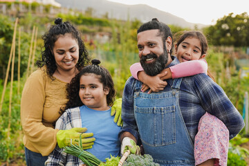 Happy indian family gardening together - Parents and children having fun outdoor - Harvest, garden and organic food concept