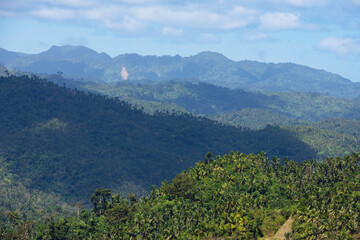Tropical jungle covered hills against blue sky. Haze over the mountains