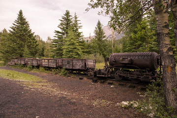 Old rusty train - steam locomotive. An abandoned coal mine overgrown with forest in the mountains....