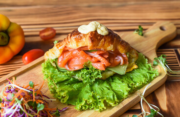 croissant wish smoked salmon fillet and vegetables on wooden table close up side view