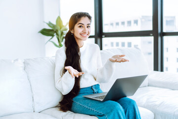 Obraz premium Successful startup. Cheerful young business woman sitting on white couch in spacious bright office demonstrating excellent results in business or completed project.