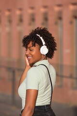 Latin American teenage girl with curly hair listening to music on smartphone and wearing headphones