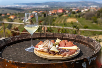A glass of wine and prosciutto, cheese and olive tapas on a wine barrel overlooking the green fields and the Adriatic