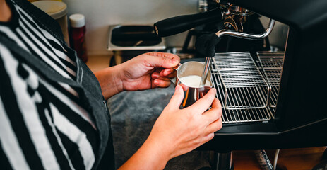 Hand of a barista in the coffee shop preparing and using a coffee machine to steam milk for a coffee menu.