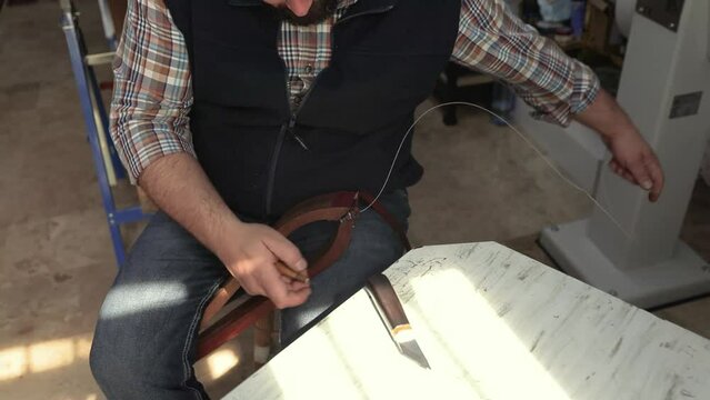 Craftsman working by hand in workshop sewing leather belt