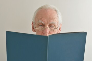 Face portrait of a gray-haired elderly man in glasses with a pensive serious look reads a book...