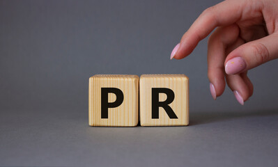 PR - Public Relations symbol. Concept word PR on wooden cubes. Businessman hand. Beautiful grey...