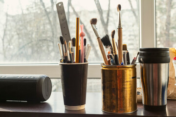The windowsill in the artist's studio is filled with old containers, tin cans and cups where...