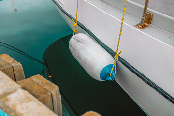 White fenders suspended between a boat and dockside for protection. Maritime fenders