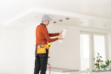 Electrician in uniform repairing ceiling lamp indoors