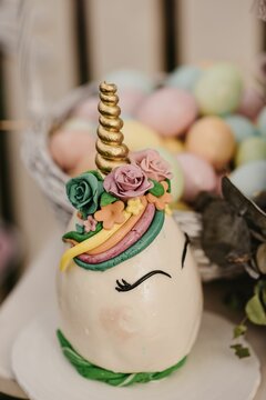 Fototapeta Vertical shot of a unicorn cake with colorful Easter eggs in the blurred background