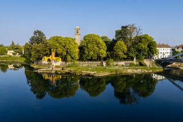 People resting on edge of the river Adda in Lombardia with green trees reflected in the waters