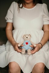 Vertical shot of a pregnant female holding a toy bear in front of her belly