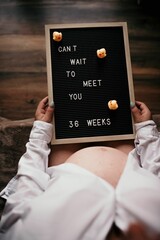 Vertical shot of a pregnant woman holding a desk with the text "can't wait to meet you, 36 weeks"