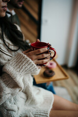 Vertical shot of female holding mug and a male with plate of donuts in a room