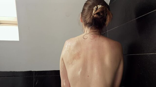 Young woman with naked back washing in shower at bathroom with window. Importance of maintaining good hygiene and self-care routines