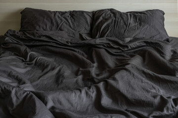 Dark satin bedding, an unmade bed