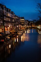 Vertical shot of Amsterdam canal at night with illuminating buildings in the evening