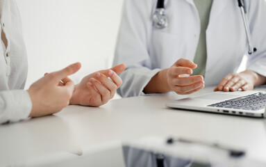 Doctor and patient discussing current health examination while sitting at the desk in clinic office, closeup. Perfect medical service and medicine concept