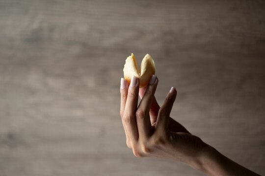 Female Hand Holding A Fortune Cookie With Wooden Background With Copy Space