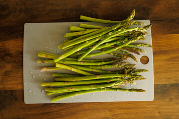 Fresh asparagus, just rinsed with drops of water, on a cutting board.