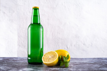 Green glass bottle and lemons with mint. Sweet sparkling water. Lemonade.