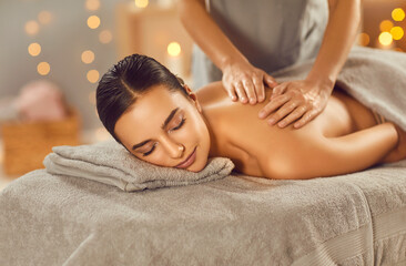 Portrait of a pretty young brunette woman with closed eyes relaxing in spa salon getting massage. Therapist doing manipulative treatment on shoulders and back. Wellness and beauty day concept