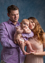 Mom and dad hold their little daughter in their arms and look at her tenderly. Love of young parents.
