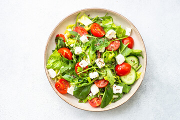 Green salad with spinach, arugula and tomatoes with olive oil. Top view on white.
