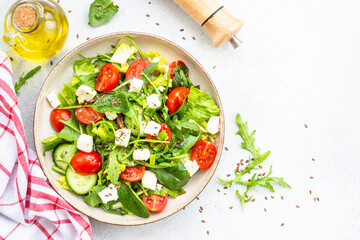 Spring salad in craft plate. Spinach, arugula, tomatoes and feta with olive oil. Top view on white.