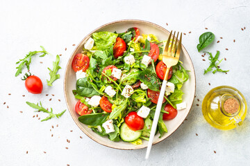 Spring salad in craft plate. Spinach, arugula, tomatoes and feta with olive oil. Top view on white.