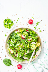 Green salad with spinach, arugula and radish with olive oil on white table. Top view with copy...