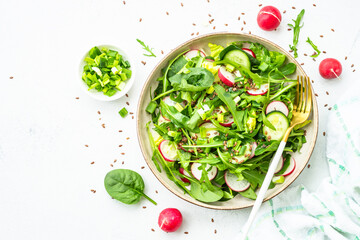 Green salad with spinach, arugula and radish with olive oil on white table. Top view with copy space.