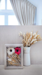 Dried flowers bouquet natural color in glass wooden frame and white ceramic vase, on wooden background, room decoration with copy space, minimalist style
