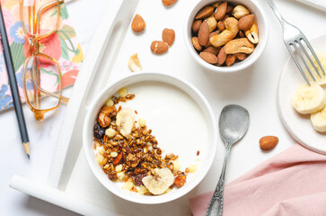 Healthy breakfast with yogurt, granola, nuts and banana on white table.