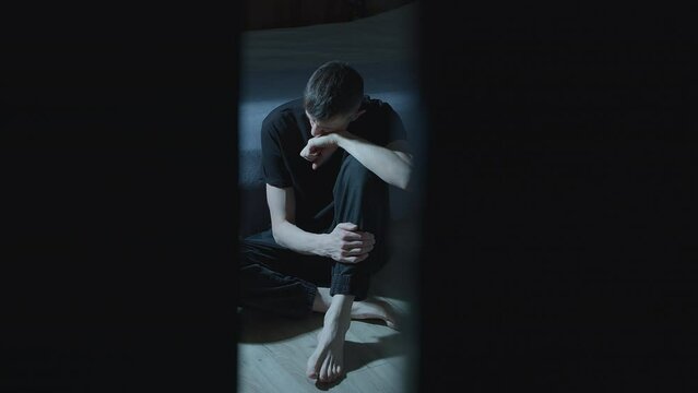 Lonely, sad man sits in a dark room. The concept of mental health. Depression.