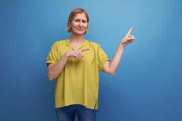 blond 50s woman showing her finger on the blank space of the wall