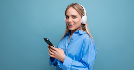 close-up of an attractive girl in wireless large headphones who knows how to relax with music on a blue background