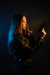 Beautiful young woman in the dark in a leather jacket with a gun in her hands. Girl in the club at night.