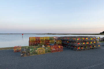 Empty, colorful crab and lobster pots stacked on a pier at dusk in front of a calm bay and clear sky, USA © Eric Dale Creative