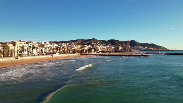 Aerial panoramic view of coastal village at seashore, old town, Sant Bartomeu i Santa Tecla de Sitges during sunny day in mediterranean town of Sitges, Province of Barcelona, Spain. Film intro. 4K