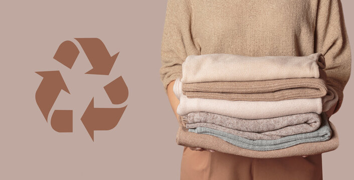 Woman holding stack of clothes with used wardrobe for reuse and circular economy logo on beige background. Reusing, recycling materials and reducing waste in fashion, second hand apparel idea